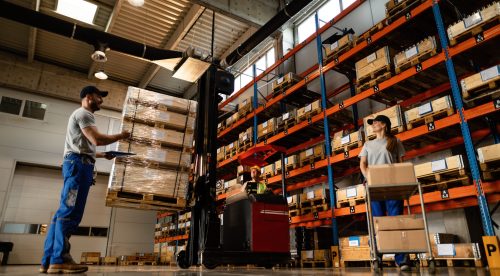 Low angle view of happy warehouse workers communicating while working with shipment in industrial storage compartment.